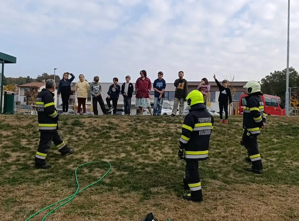 Eine Gruppe von Feuerwehrleuten demonstriert eine Brandschutzübung auf einem Grashügel.