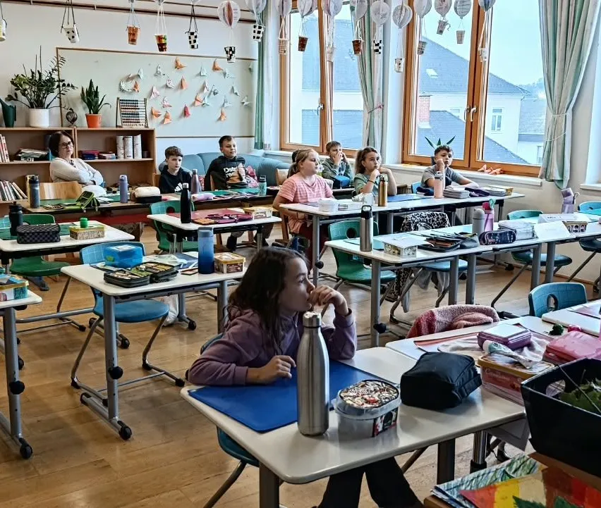 Ein Klassenzimmer mit Schülern, die an ihren Tischen sitzen, ein Mädchen schaut auf etwas auf ihrem Schreibtisch.
