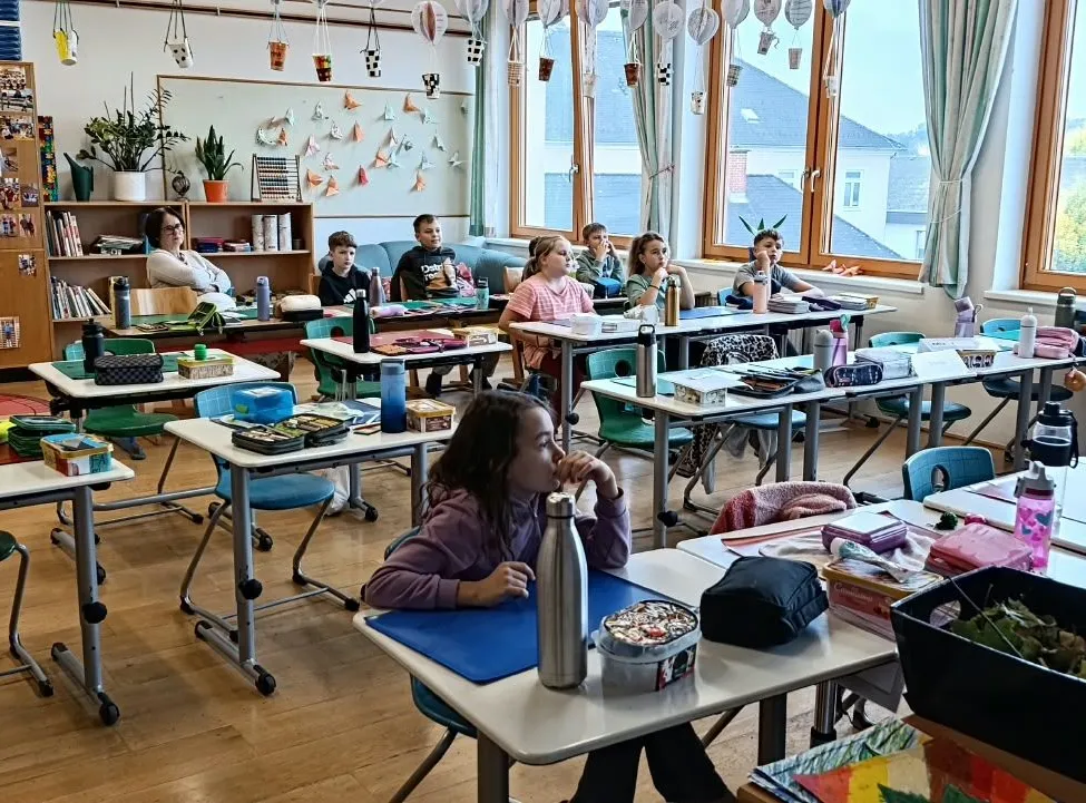 Ein Klassenzimmer mit Schülern, die an ihren Tischen sitzen, ein Mädchen schaut auf etwas auf ihrem Schreibtisch.