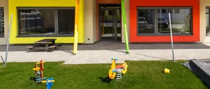 Ein farbenfrohes Gebäude mit einem Spielplatz davor, mit einem Picknicktisch und einer Rutsche.