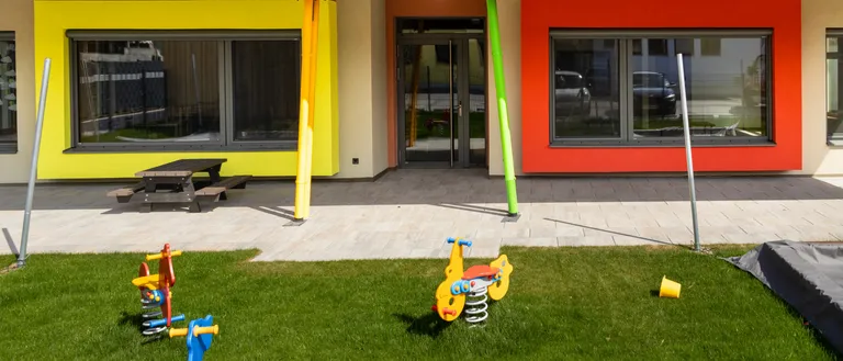 Ein farbenfrohes Gebäude mit einem Spielplatz davor, mit einem Picknicktisch und einer Rutsche.
