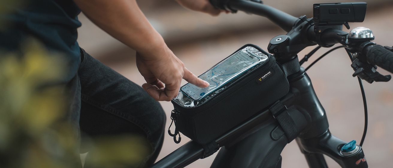 Ein Radfahrer hält ein Smartphone in einer wasserdichten Tasche an seinem Fahrrad und zeigt eine Karte an.