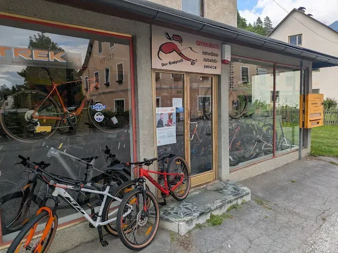 Ein Fahrradgeschäft mit mehreren Fahrrädern vor der Tür. Das Schild des Geschäfts steht für 'Trek' und 'American Bicycle Technology'. Drinnen sind Fahrräder ausgestellt.