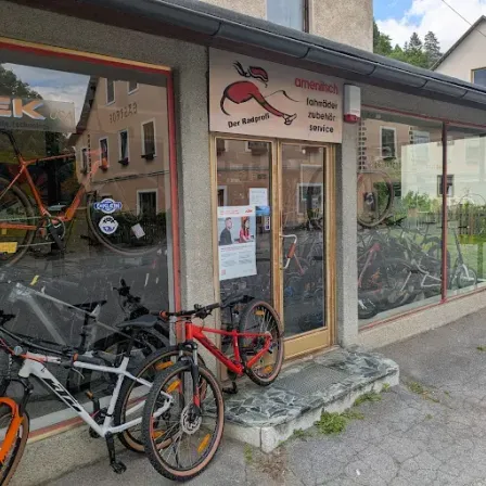 Ein Fahrradgeschäft mit mehreren Fahrrädern vor der Tür. Das Schild des Geschäfts steht für 'Trek' und 'American Bicycle Technology'. Drinnen sind Fahrräder ausgestellt.