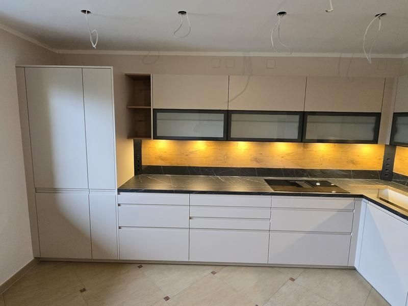 Eine moderne Küche mit weißen Schränken, Glastüren und Marmorarbeitsplatten. Die Arbeitsplatten haben gelbe Beleuchtung darunter.