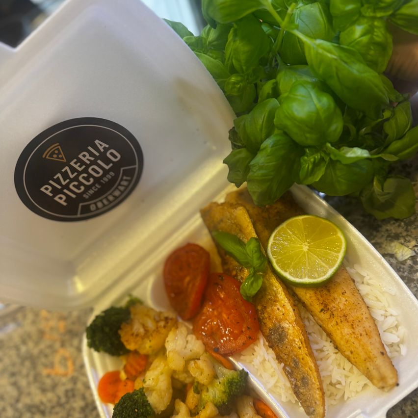 Ein Lebensmittelbehälter mit Fisch, Reis und Gemüse. Eine Basilikumpflanze ist an der Seite, und ein Logo ist auf dem Behälter.