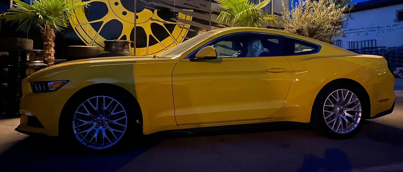 Ein gelber Sportwagen ist vor einem Gebäude mit einem großen gelben Radlogo und dem Text 'FELGENSERVICE.INFO' geparkt. Das Auto steht auf einer Straße bei Nacht.
