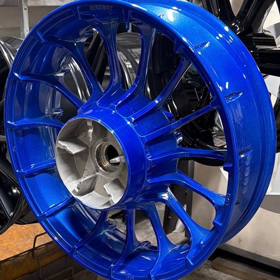 Eine Nahaufnahme eines blauen Leichtmetallrads mit silberner Mitte, umgeben von anderen Rädern in einer Werkstatt.