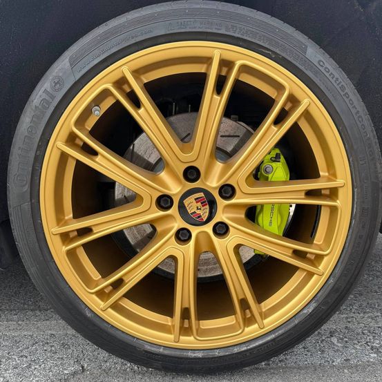 Eine Nahaufnahme eines schwarzen Autorads mit goldenen Speichen und einem gelben Bremssattel. Die Felge zeigt das Porsche-Logo.