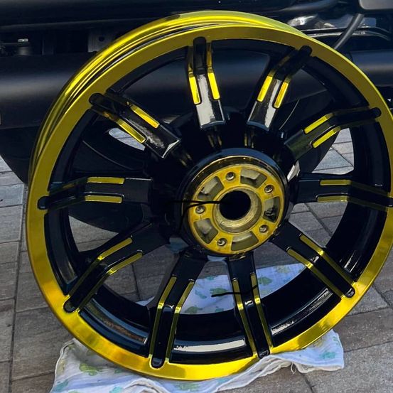 Eine Nahaufnahme eines Motorradrads mit gelben und schwarzen Speichen auf einem gefliesten Boden, mit einem sauberen Tuch in der Nähe.