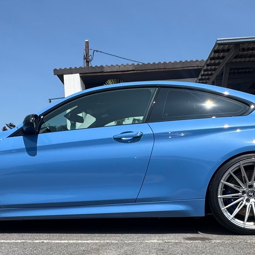 Ein blauer Sportwagen mit glänzendem Finish ist vor einem Gebäude unter blauem Himmel geparkt.