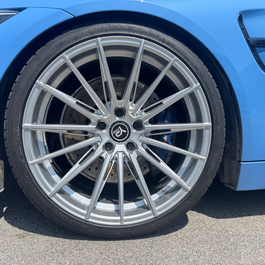 Nahaufnahme eines blauen Sportwagen-Rads mit silbernen Leichtmetallfelgen und einer silbernen Radnabe mit Logo.