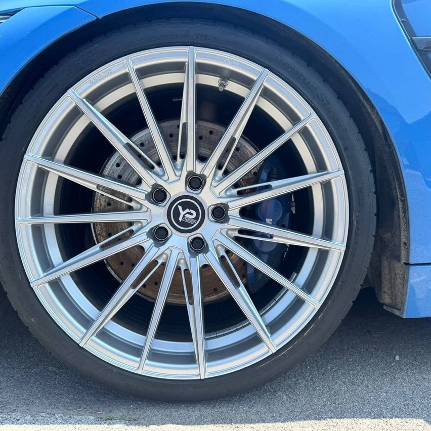 Ein Nahaufnahme eines blauen Sportwagens, der ein silbernes Leichtmetallrad mit einem schwarzen Reifen zeigt. Das Rad hat eine silberne Radkappe mit einem Logo in der Mitte.