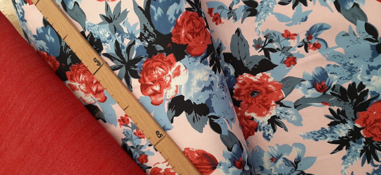 Close-up of a fabric with floral print, featuring red roses, blue petals, and green leaves. A wooden ruler is placed on the fabric.