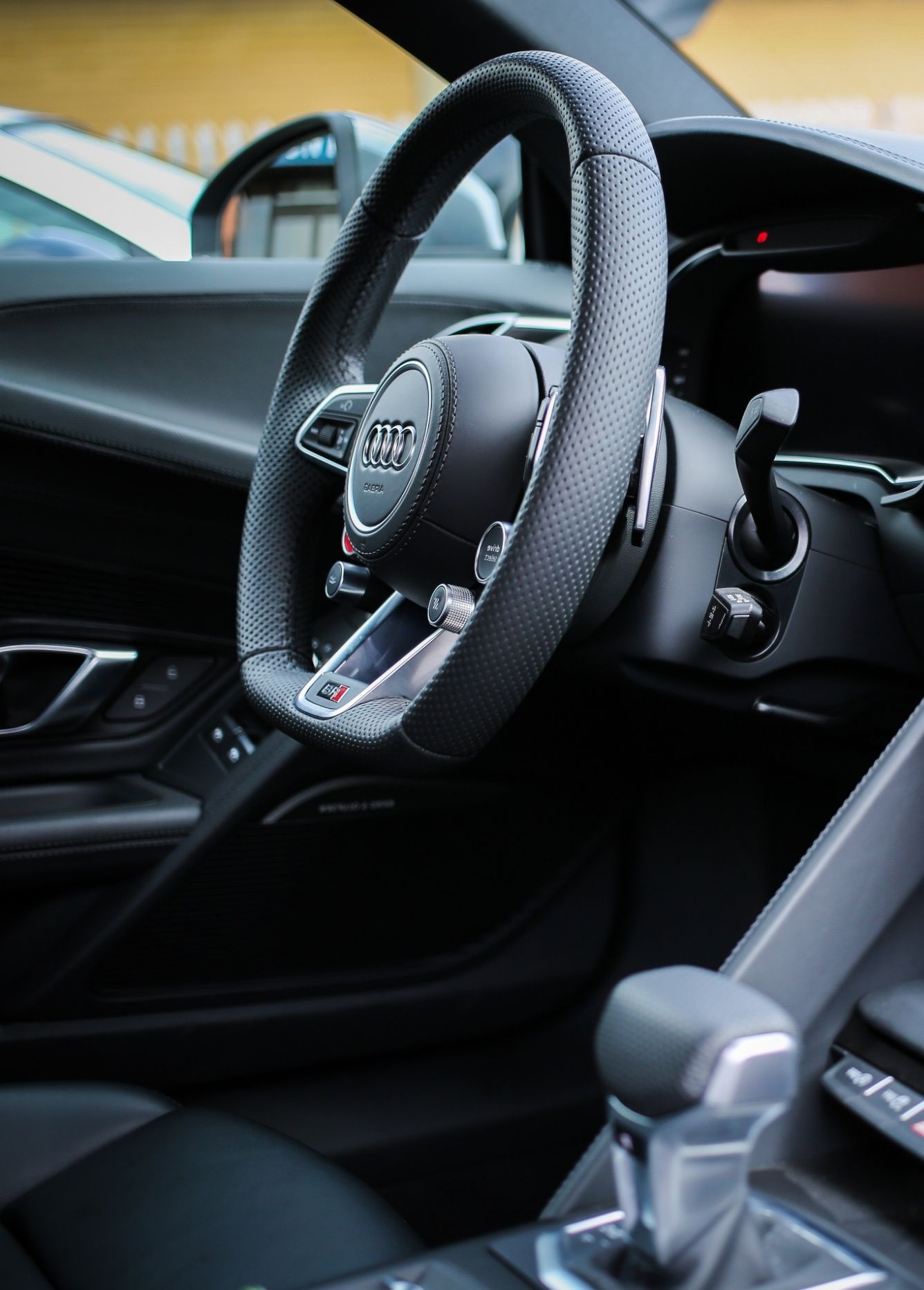 Nahaufnahme des schwarzen Lederlenkrads eines Audi-Autos mit silbernen Akzenten und verschiedenen Steuerknöpfen.