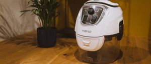 Ein weißer Vivenso Luftreiniger steht auf einem Holztisch neben einem Topf mit grünen Blättern.