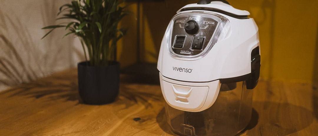 Ein Vivenso-Gerät steht neben einem Topf auf einer Holzfläche. Das Gerät ist weiß mit schwarzen Akzenten und hat einen durchsichtigen Behälter.