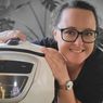 A woman wearing glasses holds a white appliance, possibly a rice cooker, with a 'Made in Germany' label. She smiles and poses for a photo.