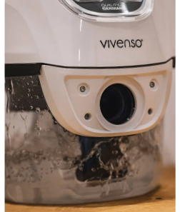 Nahaufnahme eines weißen Vivenso-Geräts mit Linse, Wassertropfen und schwarzem Rahmen, auf einer Holzoberfläche platziert.