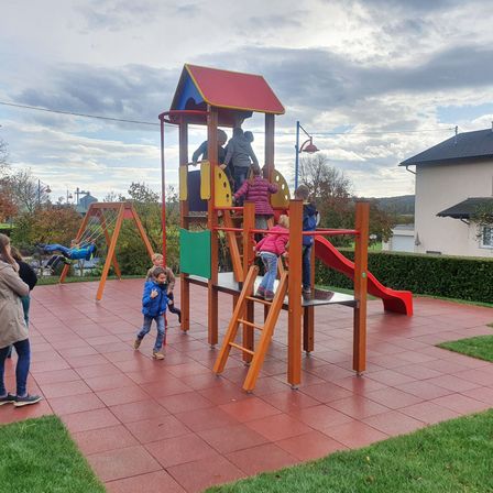 Ein Spielplatz mit Rutsche und Klettergerüst. Kinder spielen und einige Erwachsene stehen herum.