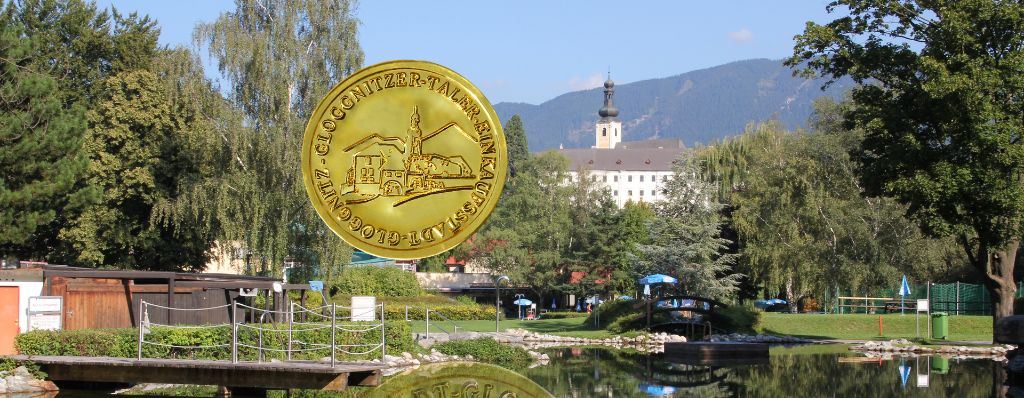 Eine goldene Münze mit Schlossdesign schwebt über einem ruhigen See. Im Hintergrund steht ein großes Gebäude mit Turm vor einer Bergkulisse.