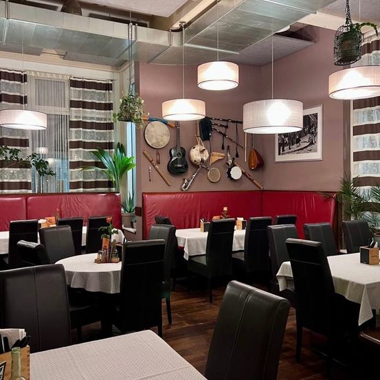 Ein leeres Restaurant mit Holzböden, Tischen, Stühlen und Lampen. Musikinstrumente hängen an der Wand. Es gibt auch Pflanzen und einen Bilderrahmen.