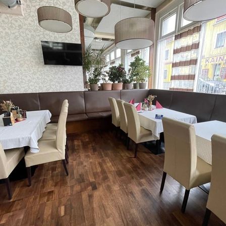 Ein leerer Essbereich mit Holzböden, Tischen und Stühlen. Topfpflanzen und ein Fernseher an der Wand.