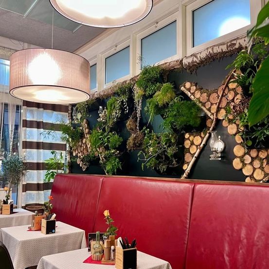 Ein Restaurant mit roten Ledersitzen und einem Tisch mit Blume und Menü. Eine Wand, die mit Pflanzen bedeckt ist, mit einer hängenden Lampe und einer Lampe an der Wand.