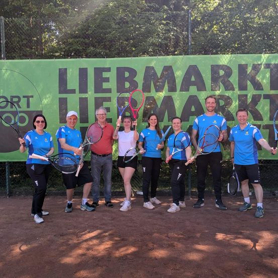 Eine Gruppe von Tennisspielern in blauen Uniformen steht auf einem Tennisplatz und hält Tennisschläger in der Hand. Hinter ihnen zeigt eine grüne Banner die Textur 'Liebemarkt' an.