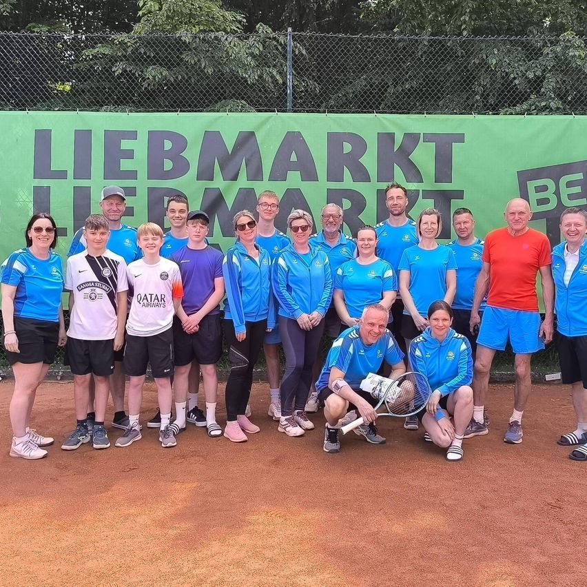 Eine Gruppe von Erwachsenen und jungen Leuten posiert für ein Foto auf einem Tennisplatz mit einem grünen Banner, das LIEBMARKT hinter ihnen steht.