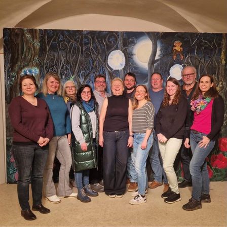 Eine Gruppe von Menschen steht vor einer großen Wandmalerei, die eine Waldszene unter einem Vollmond darstellt.