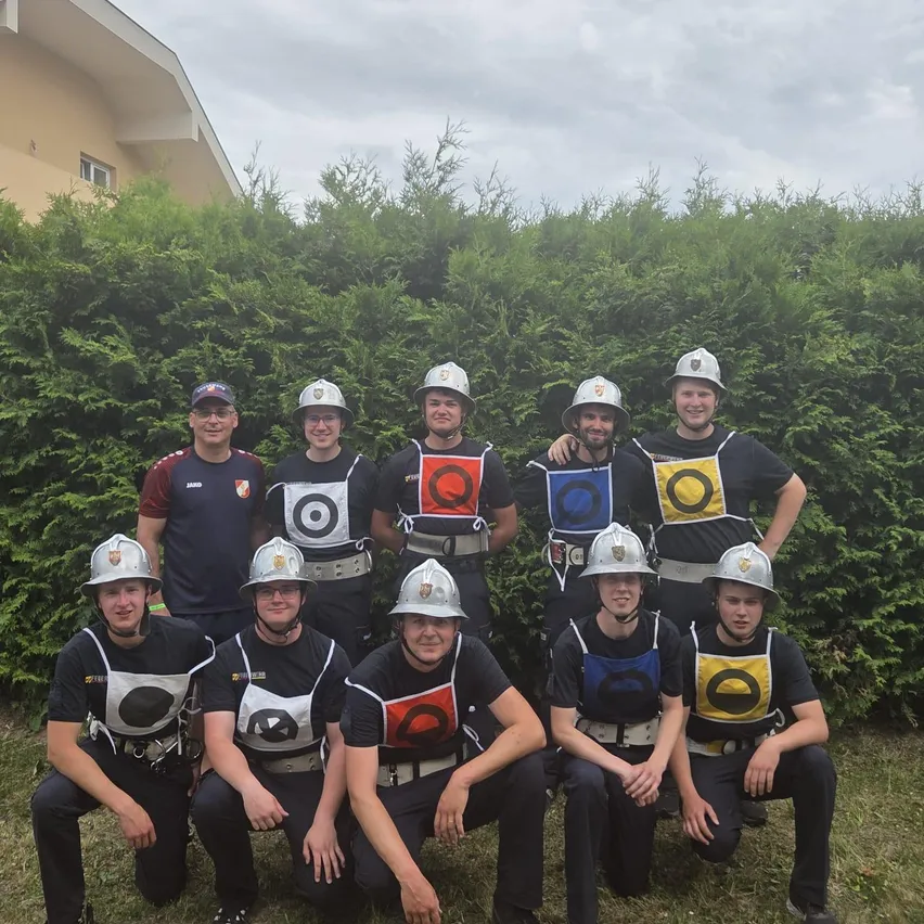 Eine Gruppe von Menschen in Uniformen, Helmen und Schutzwesten posiert für ein Foto vor einem Busch.