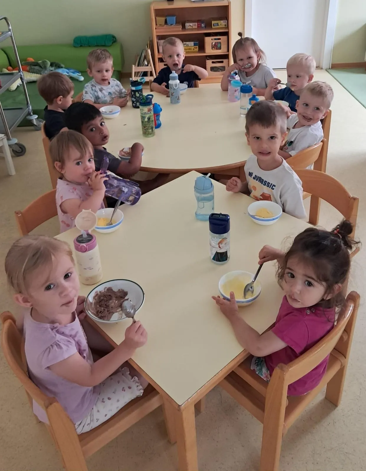 Eine Gruppe junger Kinder sitzt in einem Klassenzimmer um einen Tisch herum und isst. Flaschen und Schüsseln stehen auf dem Tisch.