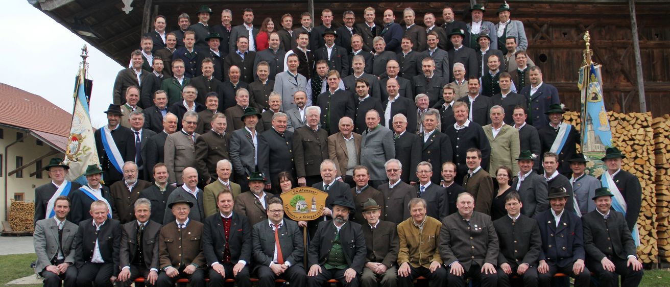 Eine Gruppe von Männern und Frauen in traditioneller Kleidung posiert für ein Foto vor einem Holzgebäude.