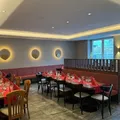 Ein leeres Restaurant mit mehreren runden Tischen, die mit roten Servietten und Weingläsern gedeckt sind. Die Wände sind mit drei kreisförmigen Lichtern verziert.