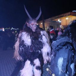 Eine Person, die als Dämon mit Hörnern und einer gruseligen Maske verkleidet ist, geht bei Nacht in einer Menschenmenge.