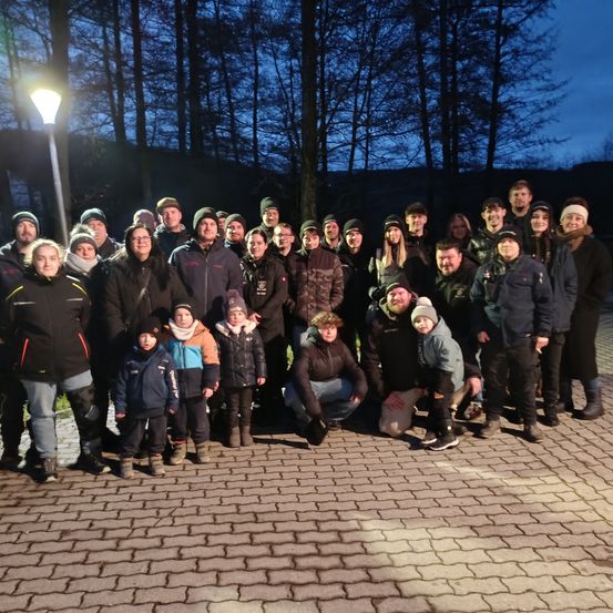 Eine Gruppe von Menschen, Erwachsene und Kinder, in Winterkleidung, posiert für ein Foto in einem bewaldeten Gebiet bei Nacht.