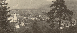 Ein Sepia-gefärbtes Foto eines Dorfes am Fuße der Berge. Ein Kirchturm ragt zentral heraus. Bäume und Häuser säumen die Landschaft.