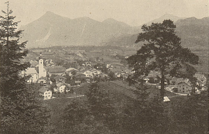 Ein Sepia-gefärbtes Foto eines Dorfes am Fuße der Berge. Ein Kirchturm ragt zentral heraus. Bäume und Häuser säumen die Landschaft.