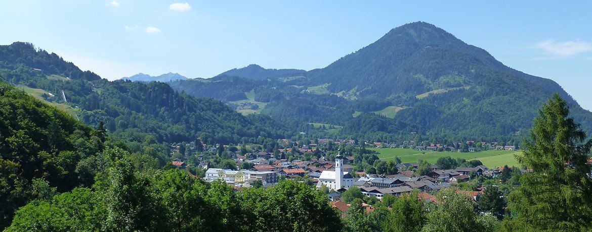 Eine Stadt mit vielen Gebäuden liegt in einem Tal, umgeben von grünen Feldern und Bergen.