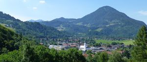 Eine Stadt mit vielen Gebäuden liegt in einem Tal, umgeben von grünen Feldern und Bergen.
