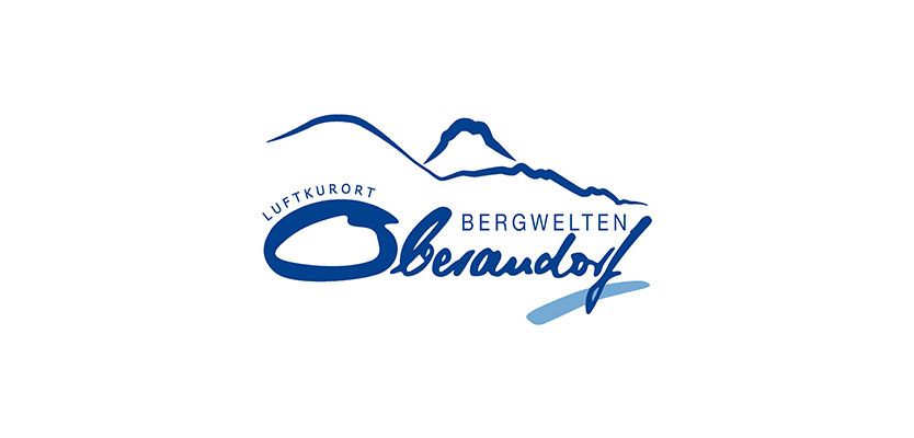 Das Logo für Bergwelten Luftkurort Oberndorf, mit einer Bergkette und blauem und weissem Text.