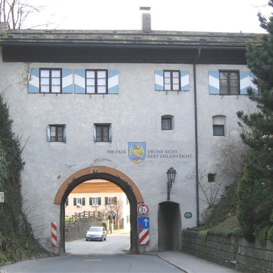 Ein weißes Auto fährt durch einen Tunnel vor einem Gebäude mit blau-weißen Fensterläden und einem Schild mit der Aufschrift 'Hie Falk' und 'Frumb Sicht Guetz Zieluns Richt'.