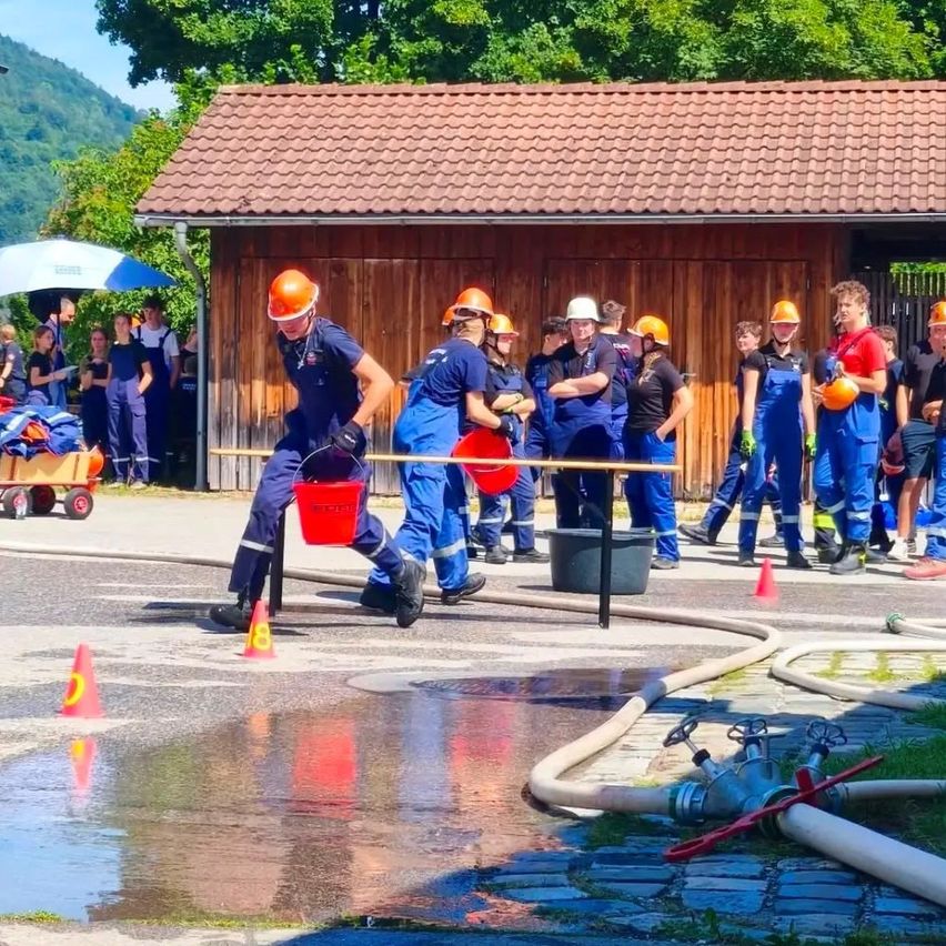 Eine Gruppe von Feuerwehrleuten in blauen Uniformen und Helmen nimmt an einem Wasserstaffelrennen teil, während Zuschauer zuschauen.