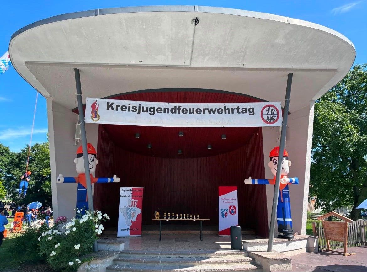 Eine Bühneneinrichtung für die Kreisjugendfeuerwehrtag-Veranstaltung mit zwei großen aufblasbaren Figuren, einem Schachset auf einem Tisch und einem Banner mit dem Veranstaltungsnamen.
