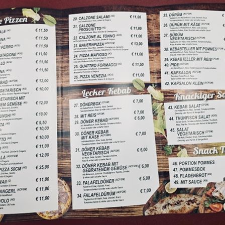 Menü mit Pizza-, Kebab- und Snackoptionen. Pizzapreise reichen von 11,50 bis 25,00 Euro. Kebabpreise reichen von 6,00 bis 7,00 Euro. Snackoptionen umfassen verschiedene Salate und Saucen.