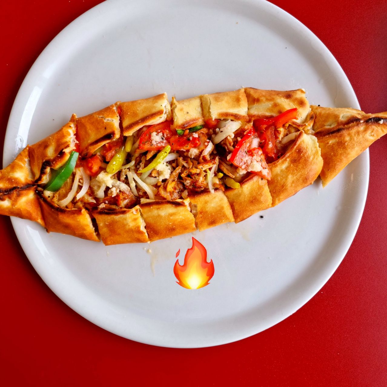 Eine würzige, geschnittene Brotpizza mit verschiedenen Belägen, einschließlich Tomaten, Paprika und Käse, serviert auf einem weißen Teller mit rotem Hintergrund.