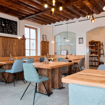 Ein rustikales Restaurant mit Holztischen, Bänken und Stühlen. Der Raum verfügt über Holzdecken mit Lampen und einer Tafel an der Wand.