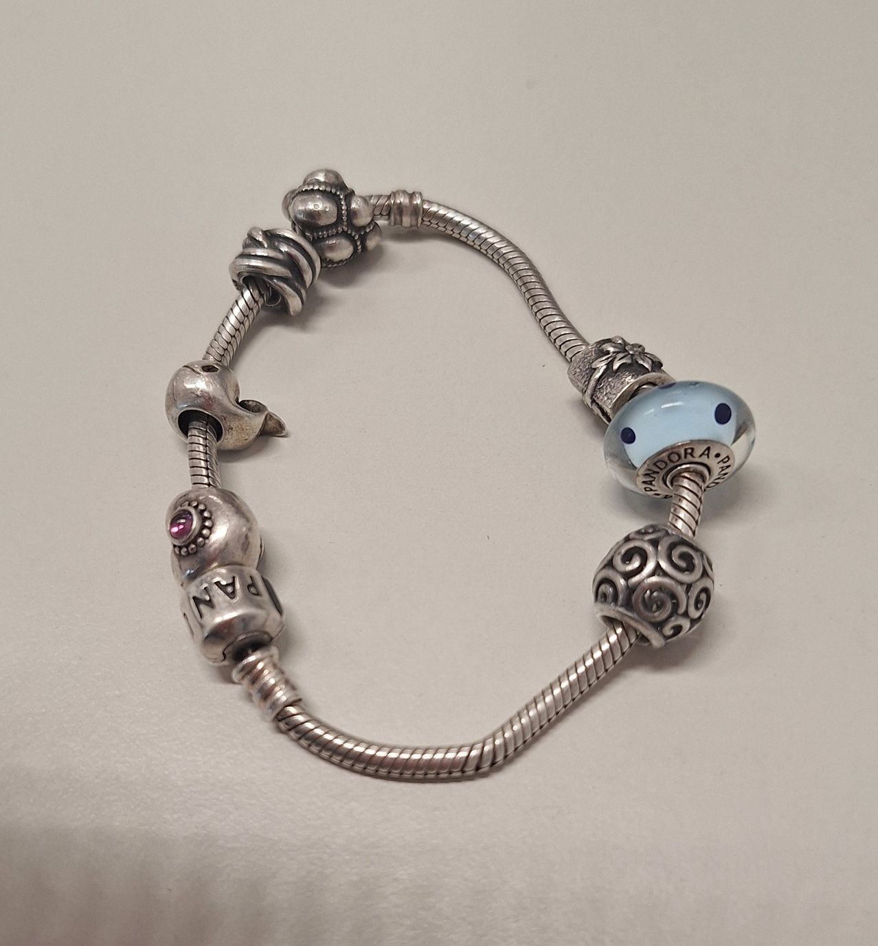 Eine silberne Armkette mit Pandora-Anhängern, einschließlich einer hellblauen Perle mit schwarzen Flecken und einem rosa Edelstein.