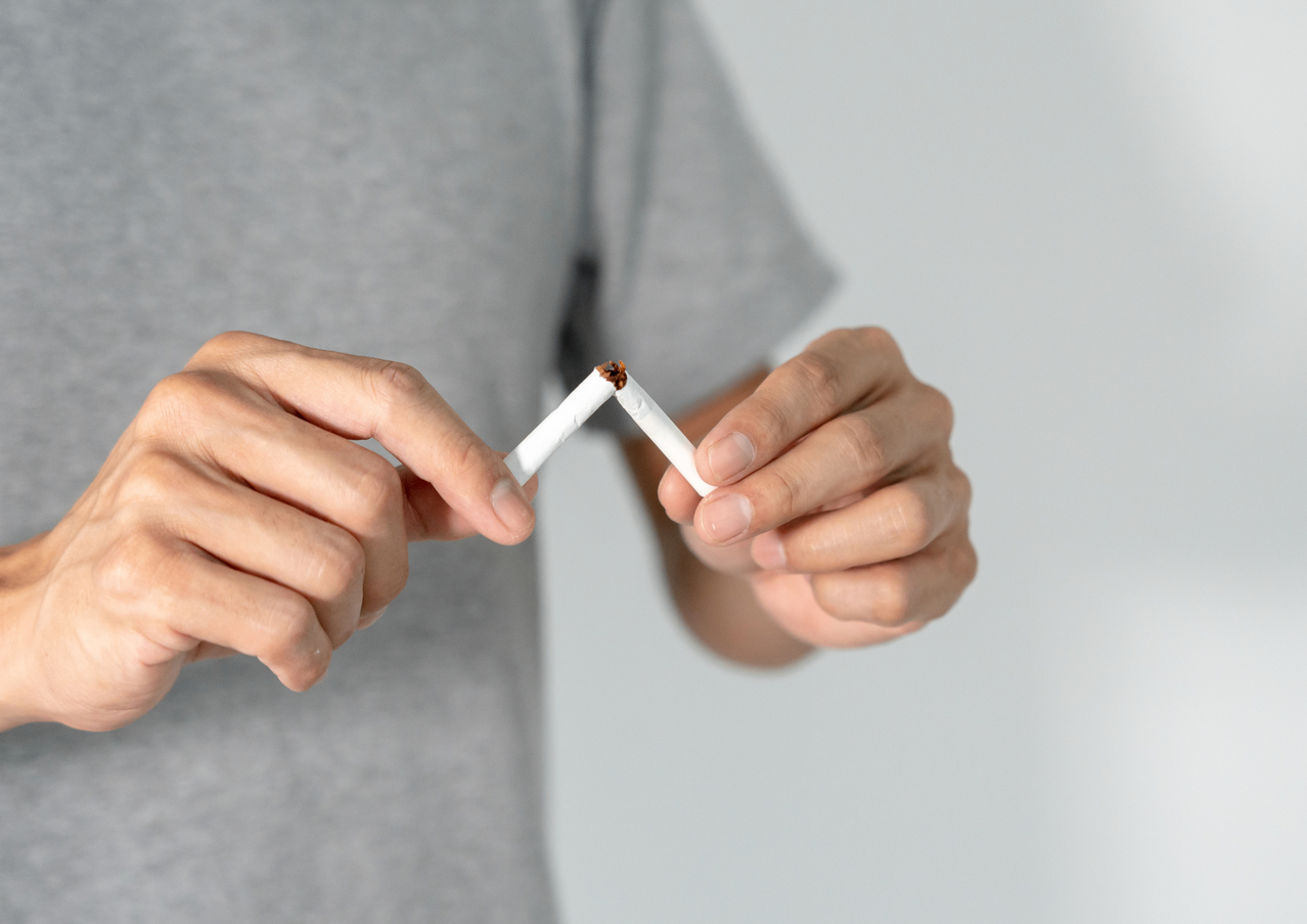 Eine Person in einem grauen T-Shirt bricht eine Zigarette mit den Händen in zwei Stücke.